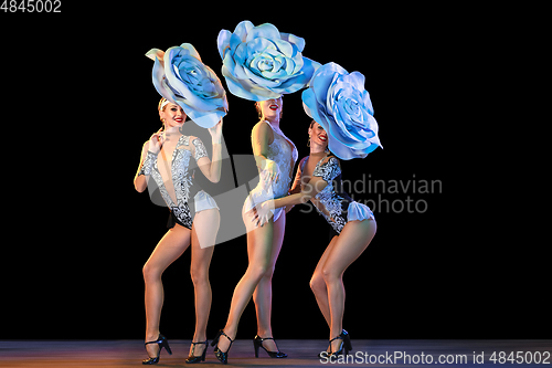 Image of Young female dancers with huge floral hats in neon light on black background