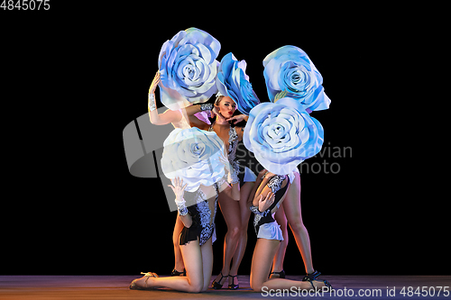 Image of Young female dancers with huge floral hats in neon light on black background