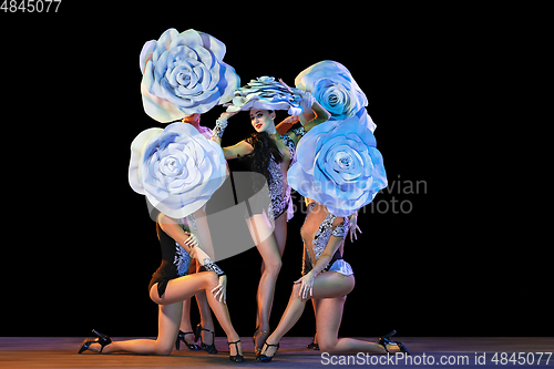 Image of Young female dancers with huge floral hats in neon light on black background