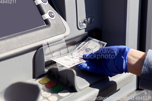 Image of hand in medical glove with money at atm machine