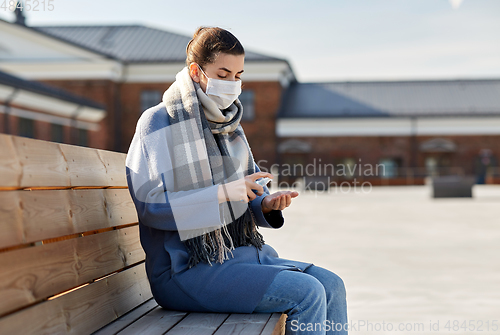 Image of woman in mask spraying hand sanitizer outdoors