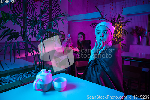 Image of Beautiful girl with a pearl earring taking lunch in modern cafe, restaurant in neon light