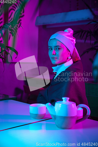 Image of Beautiful girl with a pearl earring taking lunch in modern cafe, restaurant in neon light