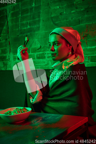 Image of Beautiful girl with a pearl earring taking lunch in modern cafe, restaurant in neon light