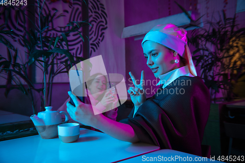 Image of Beautiful girl with a pearl earring taking lunch in modern cafe, restaurant in neon light