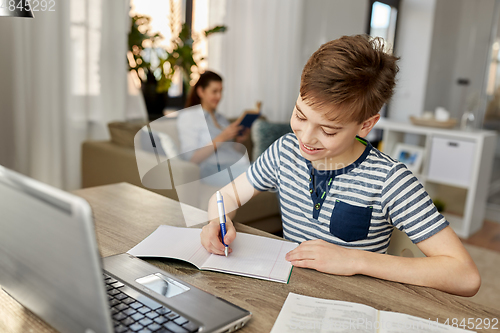 Image of student boy with book writing to notebook at home