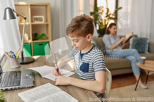 Image of student boy with book writing to notebook at home