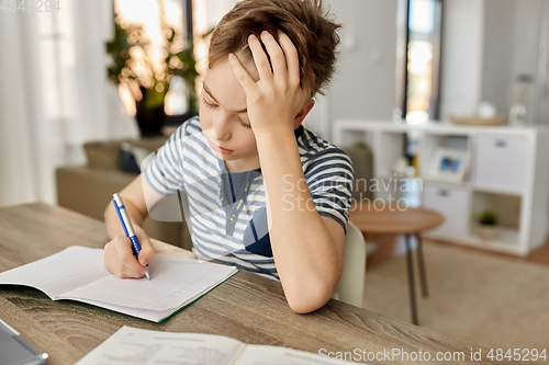 Image of student boy with book writing to notebook at home