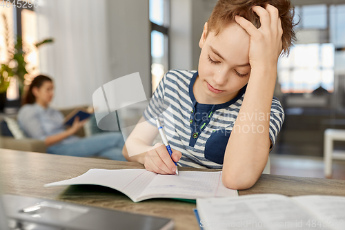 Image of student boy with book writing to notebook at home