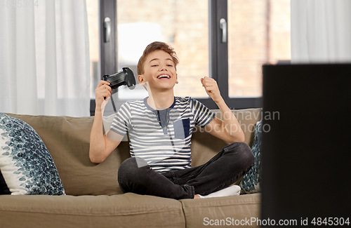 Image of happy boy with gamepad playing video game at home