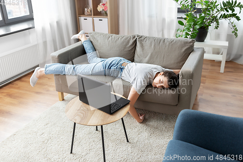 Image of bored woman with laptop lying on sofa at home