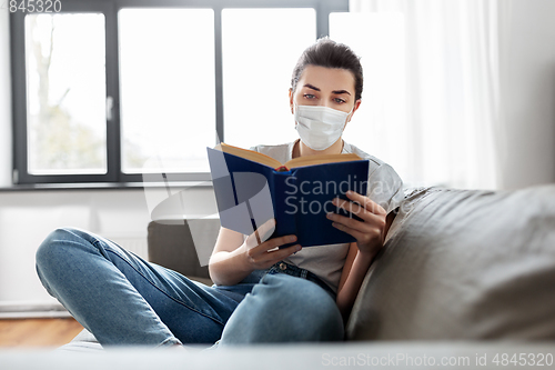 Image of sick woman in medical mask reading book at home