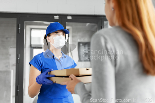 Image of delivery girl in mask giving pizza boxes to woman