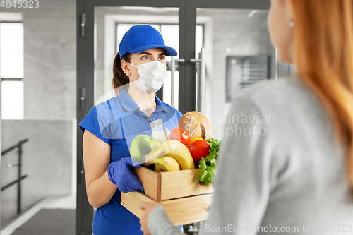 Image of delivery girl in mask giving box of food to woman