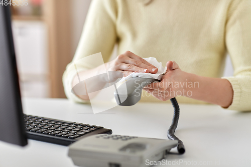 Image of close up of woman cleaning desk phone with tissue