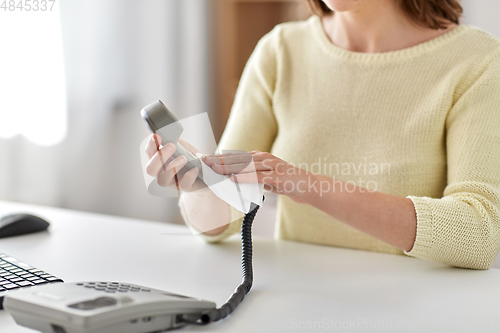 Image of close up of woman cleaning desk phone with tissue