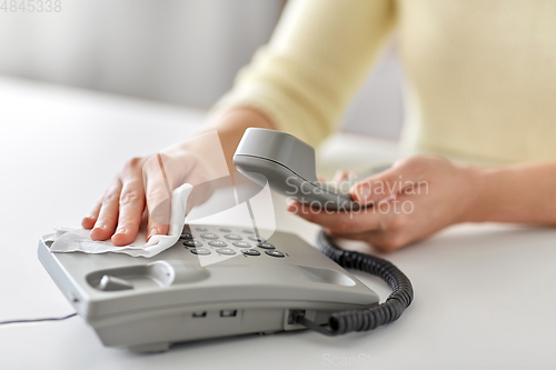 Image of close up of woman cleaning desk phone with tissue