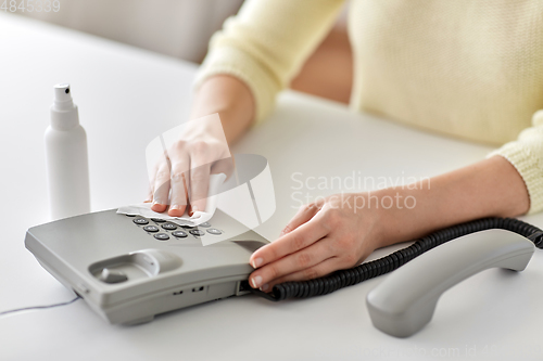 Image of close up of woman cleaning desk phone with tissue