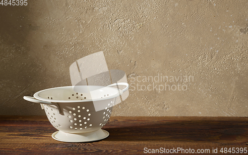 Image of white metal strainer on wooden shelf