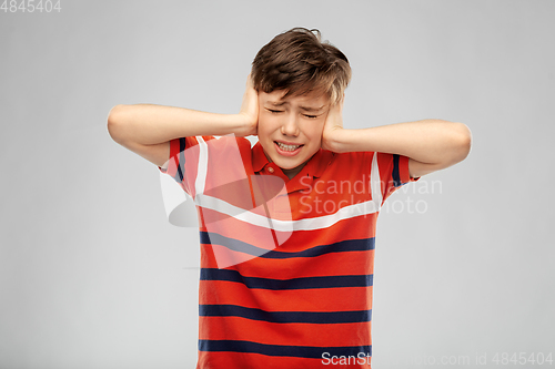 Image of boy closing ears with hands over grey background