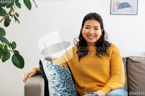 Image of smiling asian young woman sitting on sofa at home