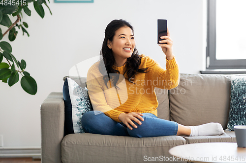 Image of asian woman taking selfie with smartphone at home