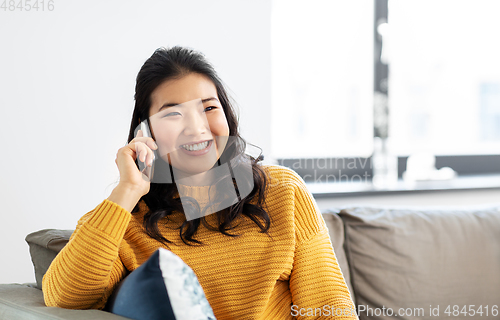 Image of smiling asian woman calling on smartphone at home