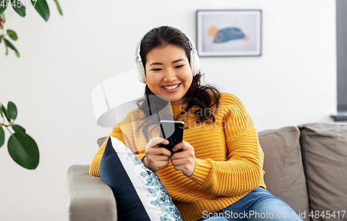 Image of asian woman with headphones and smartphone at home