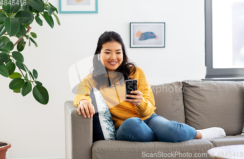 Image of asian woman with earphones and smartphone at home
