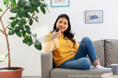 Image of asian woman with tv remote sitting on sofa at home