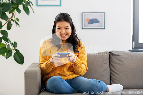 Image of asian woman with gamepad playing game at home