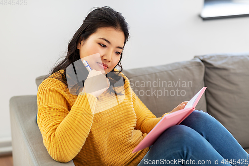 Image of asian woman with diary sitting on sofa at home