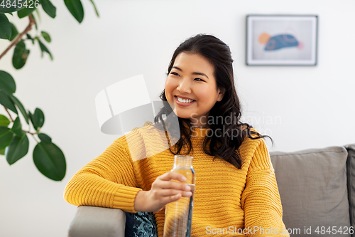 Image of smiling asian young woman drinking water at home