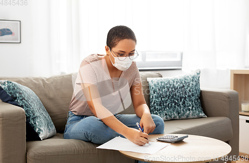 Image of woman in mask with papers and calculator at home