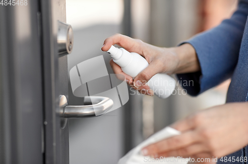 Image of hand cleaning door handle with disinfectant spray