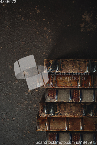 Image of Old fashioned flat lay with stack of antique leather bound books against a dark background