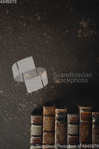 Image of Old fashioned flat lay with stack of antique leather bound books against a dark background