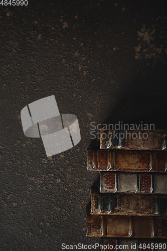 Image of Old fashioned flat lay with stack of antique leather bound books against a dark background