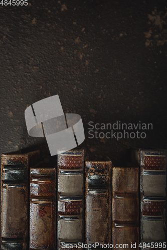 Image of Old fashioned flat lay with stack of antique leather bound books against a dark background