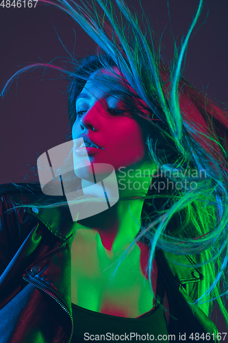 Image of Beautiful woman\'s portrait with blowing hair on dark studio background in colorful neon light