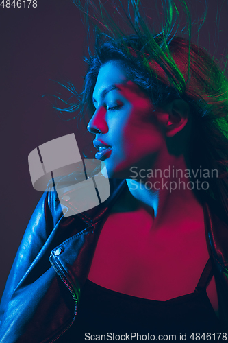 Image of Beautiful woman\'s portrait with blowing hair on dark studio background in colorful neon light