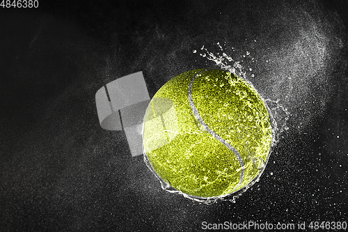 Image of Tennis ball flying in water drops and splashes isolated on black background