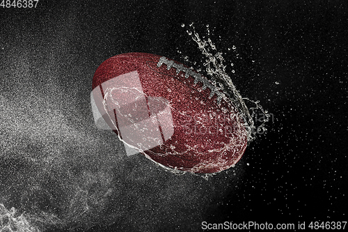 Image of American football ball flying in water drops and splashes isolated on black background