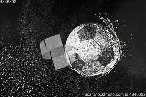 Image of Football, soccer ball flying in water drops and splashes isolated on black background