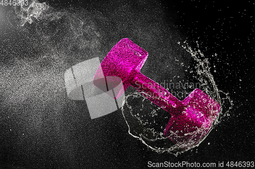 Image of Dumbbell flying in water drops and splashes isolated on black background