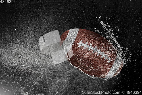 Image of American football ball flying in water drops and splashes isolated on black background