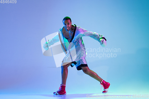 Image of High-fashion styled man in white outfit pacticing box isolted over gradient background in neon light