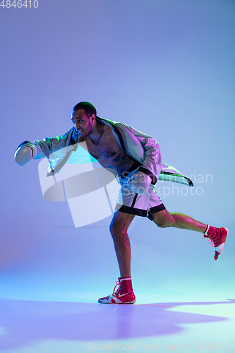 Image of High-fashion styled man in white outfit pacticing box isolted over gradient background in neon light