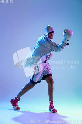 Image of High-fashion styled man in white outfit pacticing box isolted over gradient background in neon light