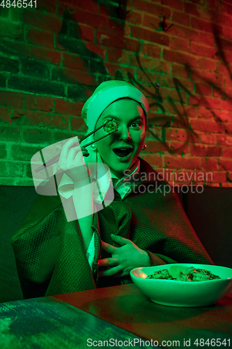 Image of Beautiful girl with a pearl earring taking lunch in modern cafe, restaurant in neon light